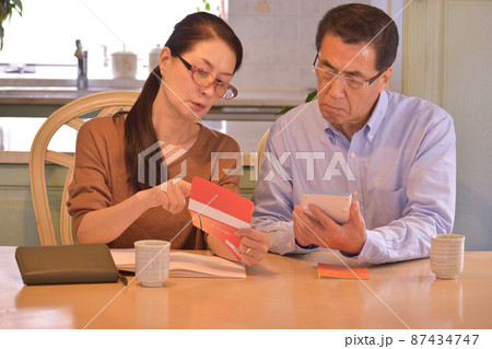 通帳を手にする妻と電卓を手にする夫、家計のやり繰りに困る年金受給のシニア夫婦 通帳を手にする妻と電卓を手にする夫、家計のやり繰りに困る年金受給のシニア夫婦 87434747