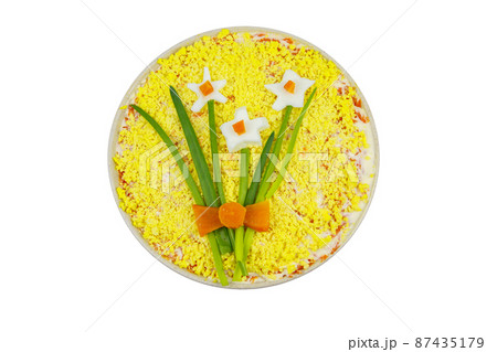 Traditional russian layered salad Mimosa with spring decoration Daffodil isolated on white background. Top view. Decoration is made of egg, green onion and carrot Traditional russian layered salad Mimosa with spring decoration Daffodil isolated on white background. Top view. Decoration is made of egg, green onion and carrot 87435179