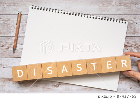 災害のイメージ｜「DISASTER」と書かれた積み木、ノート、ペン、人の手 87437765