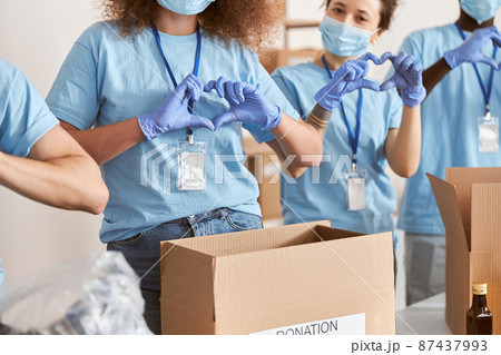 Cropped shot of diverse people wearing blue uniform, protective masks and gloves showing love heart sign while volunteering in community, sorting donated food items Cropped shot of diverse people wearing blue uniform, protective masks and gloves showing love heart sign while volunteering in community, sorting donated food items 87437993