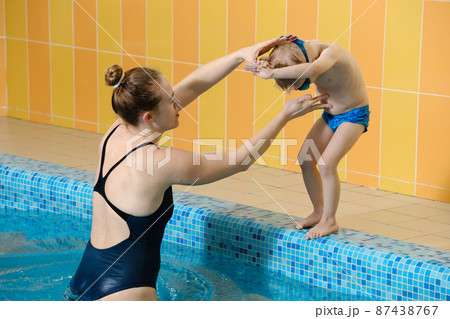 Toddler child learning to dive in indoor swimming pool with teacher. Standing on side, balancing and general physical activity for kids in water, early development. Boy kid instructed Toddler child learning to dive in indoor swimming pool with teacher. Standing on side, balancing and general physical activity for kids in water, early development. Boy kid instructed 87438767