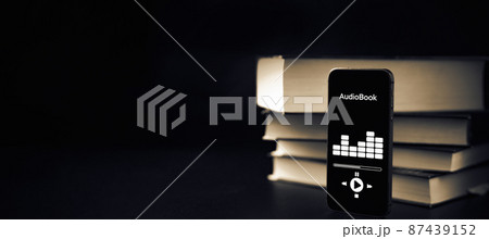 Audiobooks concept. Smartphone screen with audiobook application on paper books black background. Concept of education, library, students. Audiobooks concept. Smartphone screen with audiobook application on paper books black background. Concept of education, library, students. 87439152
