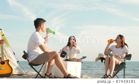 Happy friends with drinks in camp and laughing together in holidays on sand beach near camping tent vacation time at sunset Happy friends with drinks in camp and laughing together in holidays on sand beach near camping tent vacation time at sunset 87439191