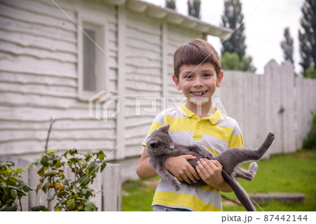 Funny boy hugging a cat with lots of love. Portrait of child holding on hands a Kitten. Playing with a cat on village countryside 87442144