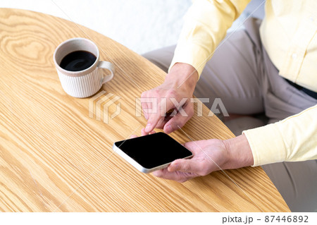 ウッドテーブルでスマホを使うミドル男性の手元【パーツカット】 87446892