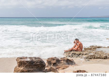 Nude male sitting on rocks near sea Nude male sitting on rocks near sea 87447380