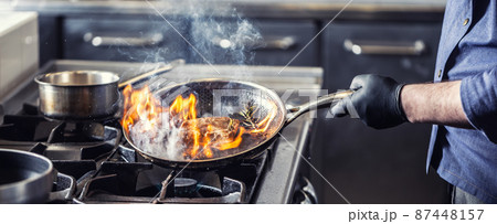 Chef in the kitchen leans pan to the side for alcohol in it to catch fire for gas stove, starting to flambe the food 87448157