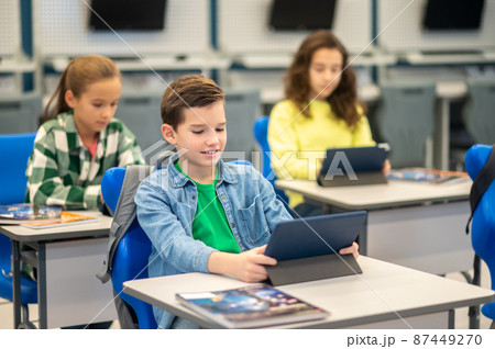 Boy and girls sitting at desk looking at tablet Boy and girls sitting at desk looking at tablet 87449270