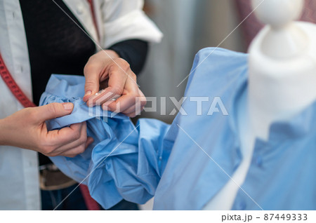 Hands of tailor with pin touching sleeve of blouse 87449333