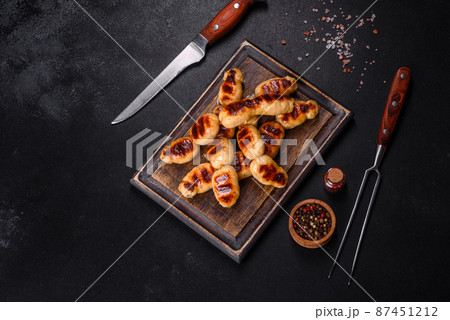 Grilled sausages with spices on a dark stone background 87451212
