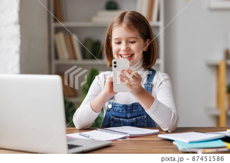 Cheerful girl doing homework and browsing smartphone Cheerful girl doing homework and browsing smartphone 87451586