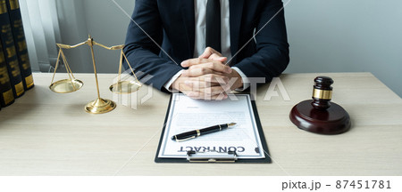 Counselor lawyer or notary working on a documents and report of the important case and wooden gavel, brass scale on table in courtroom 87451781