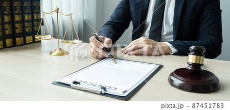 Counselor lawyer or notary working on a documents and report of the important case and wooden gavel, brass scale on table in courtroom 87451783