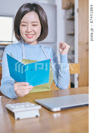 年金手帳を見てガッツポーズするエプロン姿の若い女性 年金手帳を見てガッツポーズするエプロン姿の若い女性 87451864