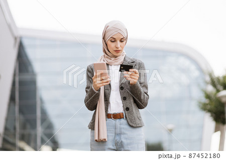 Muslim businesswoman standing on street and making purchase using credit card Muslim businesswoman standing on street and making purchase using credit card 87452180