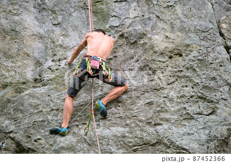 Strong male climber climbing steep wall of rocky mountain. Sportsman overcoming difficult route. Engaging in extreme sports hobby concept. 87452366