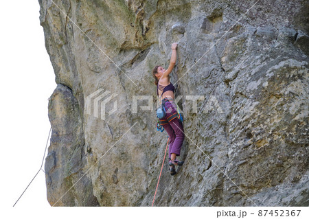 Strong female climber climbing steep wall of rocky mountain. Sportswoman overcoming difficult route. Engaging in extreme sports hobby concept. 87452367