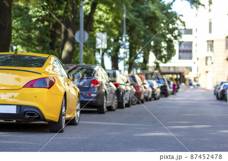 Long row of cars parking along a city road under shadow of big trees on bright summer day. Transportation, parking problems and technology concept. 87452478