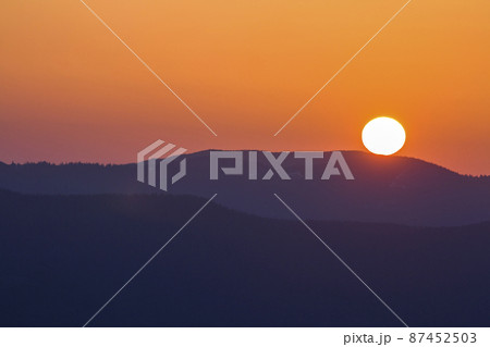 Fantastic wide panorama view of big bright white sun in dramatic orange sky over dark purple mountain range at sunset or sunrise in Carpathian mountains. Beauty and magnificence of nature concept. 87452503