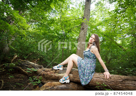 Beautiful young woman wearing elegant white dress walking on a forest path with rays of sunlight beaming through the leaves of the trees Beautiful young woman wearing elegant white dress walking on a forest path with rays of sunlight beaming through the leaves of the trees 87454048