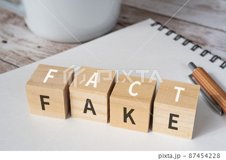フェイクニュースのイメージ｜「FACT」「FAKE」と書かれた積み木、ペン、ノート、コップ 87454228