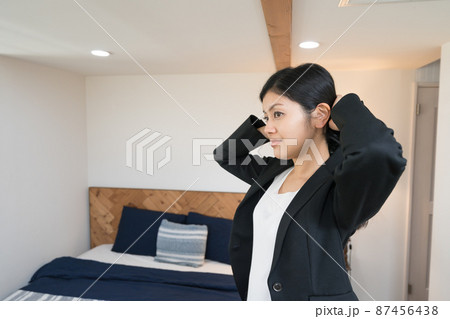 ベットルームで髪を束ねて身支度をするビジネスウーマン 87456438