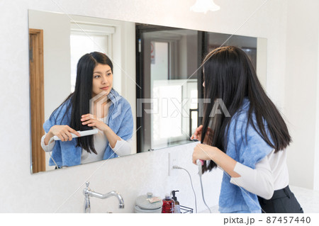鏡の前で髪にコテを当てて整髪している若い女性 87457440