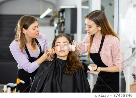 Two makeup artists apply makeup on the face of a young woman Two makeup artists apply makeup on the face of a young woman 87458846