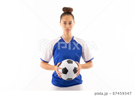 Portrait of biracial young female player holding soccer ball while standing against white background Portrait of biracial young female player holding soccer ball while standing against white background 87459347