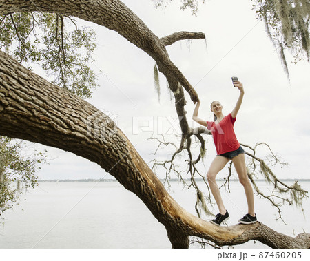 Athlete woman taking selfie on tree branch over river 87460205
