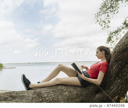 Woman sitting on tree and reading book 87460206