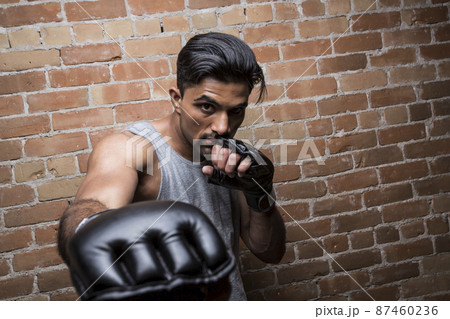 Portrait of man with boxing gloves against brick wall 87460236