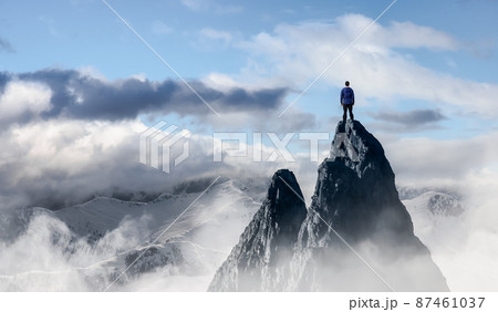 Adventurous Man Hiker standing on top of icy peak with rocky mountains 87461037