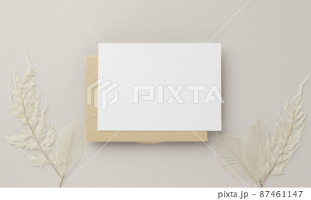 Blank greeting card invitation Mockup 5x7 on Brown envelope with dried flowers on beige background, flat lay, mockup 87461147