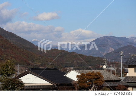 青空と雲と電線と電柱と瓦屋根の家々の町の先に連なる山の奥に雪山の見える風景 青空と雲と電線と電柱と瓦屋根の家々の町の先に連なる山の奥に雪山の見える風景 87462835