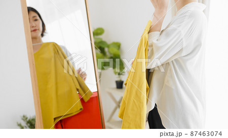鏡の前で服選びをしている若い女性　ファッションイメージ	 87463074