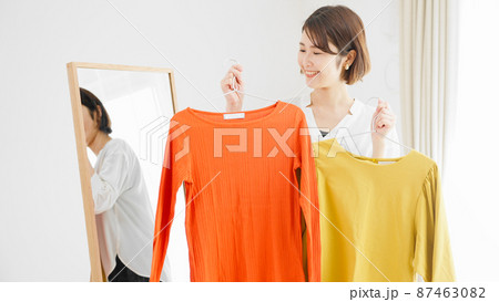 鏡の前で服選びをしている若い女性　ファッションイメージ	 87463082