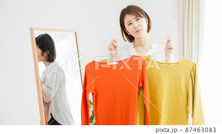 鏡の前で服選びをしている若い女性　ファッションイメージ	 87463083