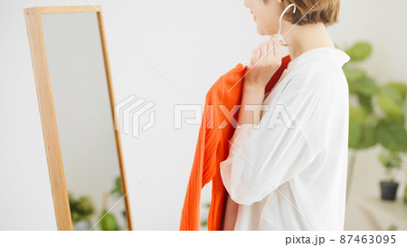 鏡の前で服選びをしている若い女性　ファッションイメージ	 87463095