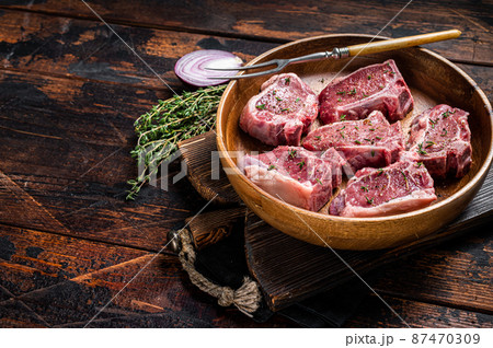Raw lamb loin rib chops steaks in wooden plate with herbs. Wooden background. Top view. Copy space Raw lamb loin rib chops steaks in wooden plate with herbs. Wooden background. Top view. Copy space 87470309
