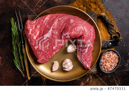 Raw tri-tip triangle roast or bottom sirloin steak on plate with herbs. Dark background. Top view 87470331