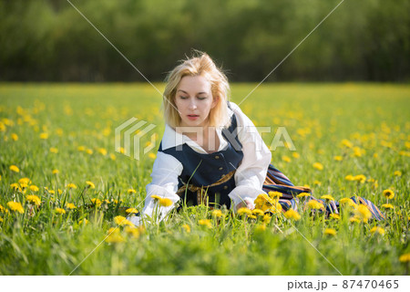 Young woman in national clothes wearing yellow dandelion wreath in spring field. Springtime 87470465