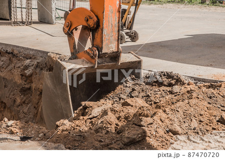 Excavation works. Tractor bucket digging with a heavy shovel on the ground at the construction site 87470720