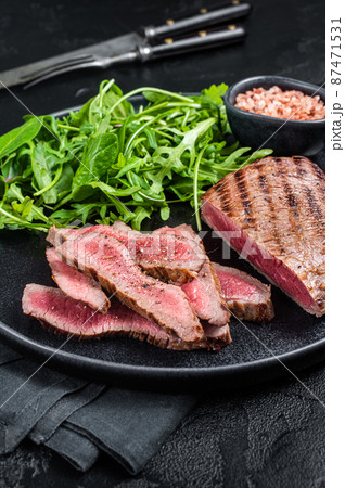 BBQ grilled Skirt Steak on a plate with green salad. Black background. Top view BBQ grilled Skirt Steak on a plate with green salad. Black background. Top view 87471531