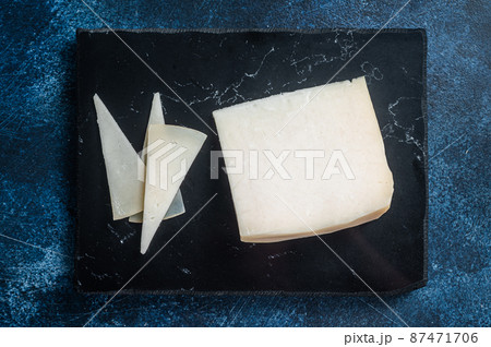 Hard goat cheese on marble board. Blue background. Top view 87471706