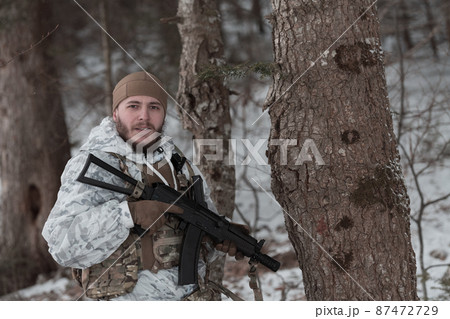 Soldier in winter camouflaged uniform in Modern warfare army on a snow day on forest battlefield with a rifle. Model face very similar to Ukraine prime minister. 87472729