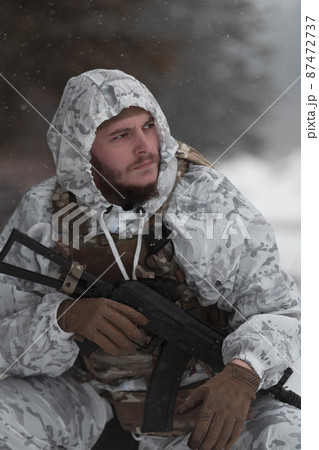Soldier in winter camouflaged uniform in Modern warfare army on a snow day on forest battlefield with a rifle. Model face very similar to Ukraine prime minister. 87472737