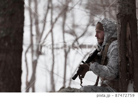 Soldier in winter camouflaged uniform in Modern warfare army on a snow day on forest battlefield with a rifle. Model face very similar to Ukraine prime minister. 87472759