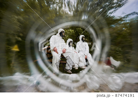View from inside plastic bottle of three people in gas masks and white protective overalls, deciding to have picnic outdoors in polluted area, holding grill grate in hand. Ecology pollution concept. 87474191