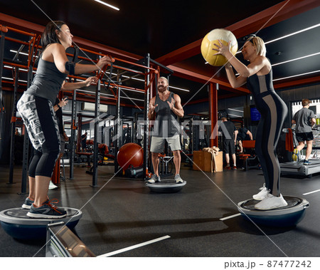 The guy tries to keep his balance on the balancing platform. Massive outdoor exercise with the help of a fitness trainer. The guy tries to keep his balance on the balancing platform. Massive outdoor exercise with the help of a fitness trainer. 87477242